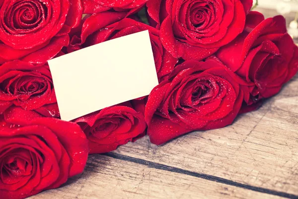 Grußkarte und rote Rosen auf Holztisch — Stockfoto
