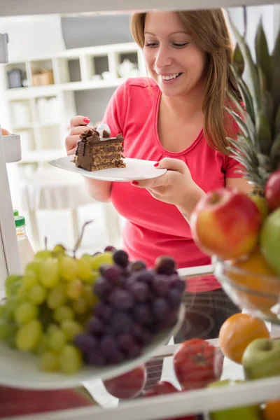 Young woman take piece of chocolate cake from fridge — Stock Photo, Image