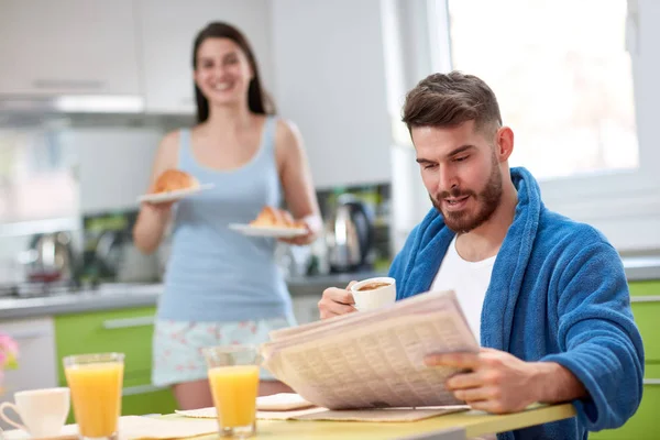 Man read newspaper and eat croissant in kitchen — Stock Photo, Image