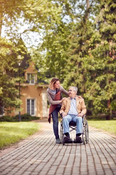 Senior im Rollstuhl genießt an einem sonnigen Tag die frische Luft mit seiner lächelnden Tochter — Stockfoto