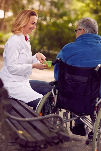 Enfermeira dando remédio para homem idoso em cadeira de rodas ao ar livre — Fotografia de Stock