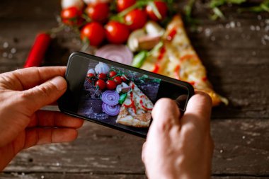 dilim pizza resim çekmek için akıllı telefon kullanan blogger adam