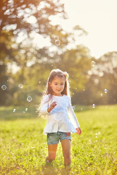 Женскому ребенку нравится гоняться за мыльными пузырями — стоковое фото