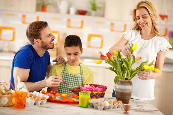 Man with son painting eggs while mother arranges tulips — Stock Photo, Image