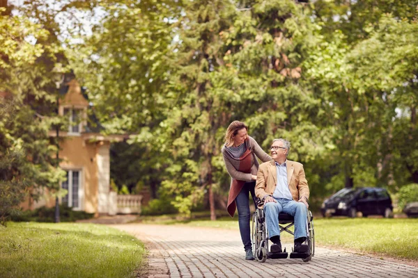 Daughter and senior man in wheelchair on walking green nature — Stock Photo, Image