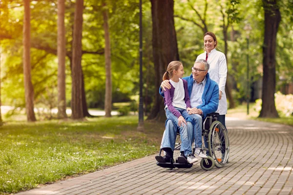 Nurse pushing senior man on wheelchair with his granddaughter — Stock Photo, Image