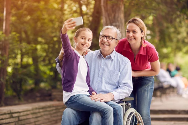 Nieta usando el teléfono para selfie con su padre discapacitado en silla de ruedas — Foto de Stock