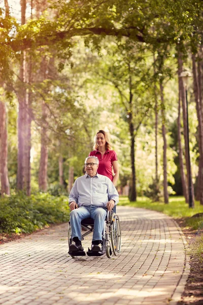 Fille dans le parc poussant profiter homme âgé en fauteuil roulant — Photo