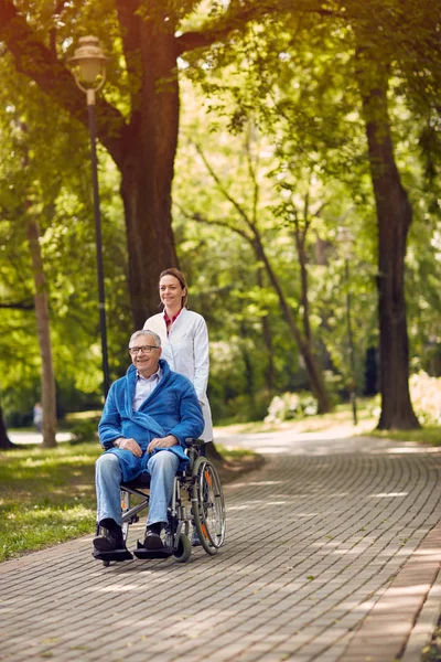 Oudere man op rolstoel met verpleegster buiten — Stockfoto