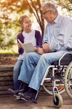 Tekerlekli sandalyede Engelli onun dedesi ziyaret ve parkta kitap okuma zevk genç torunu