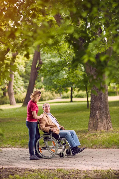Idős ember a tolószékben beszélgetett lánya a parkban — Stock Fotó