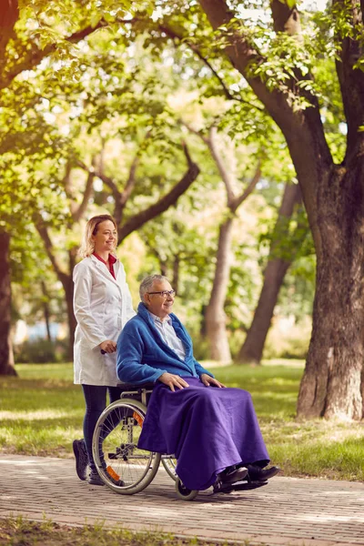 老人坐在轮椅与在公园里的护士 — 图库照片