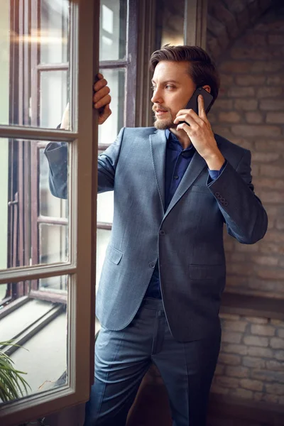 Empresário falando no celular no escritório perto da janela — Fotografia de Stock