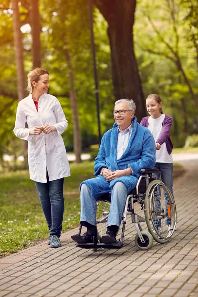 Portret van de oudere man op rolstoel met verpleegkundige en kleindochter — Stockfoto