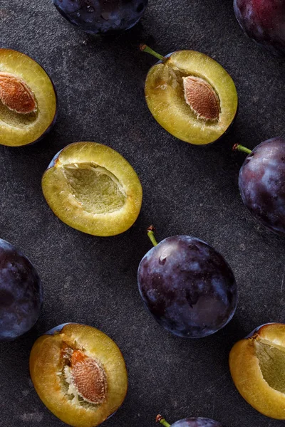 Vue de dessus sur prunes mûres, entières et tranches sur fond sombre — Photo