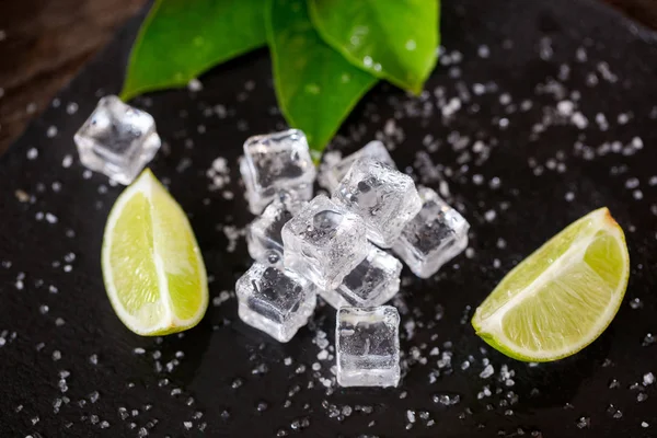 Cubetto di ghiaccio con fette di lime e sale sul tavolo scuro — Foto Stock