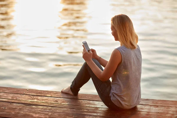 Vrouw met mobiele telefoon zit op rivieren dok — Stockfoto