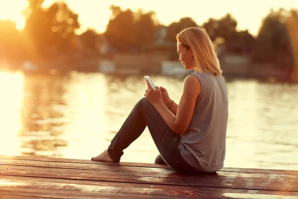 Flicka med mobiltelefon sitter på docka — Stockfoto