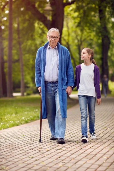Junge pflegende Enkelin spaziert mit behindertem Opa durch den Park — Stockfoto