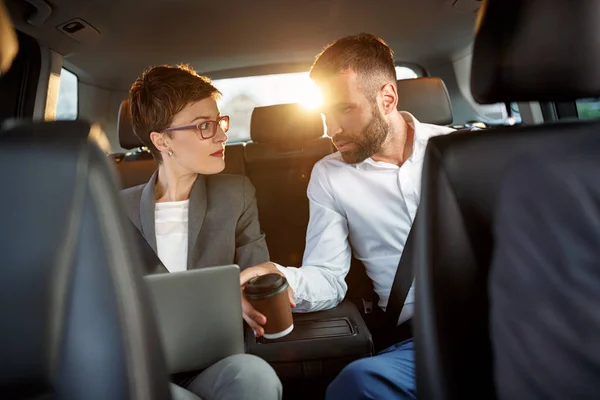 Empresário e empresária usando laptop no banco de trás do carro — Fotografia de Stock