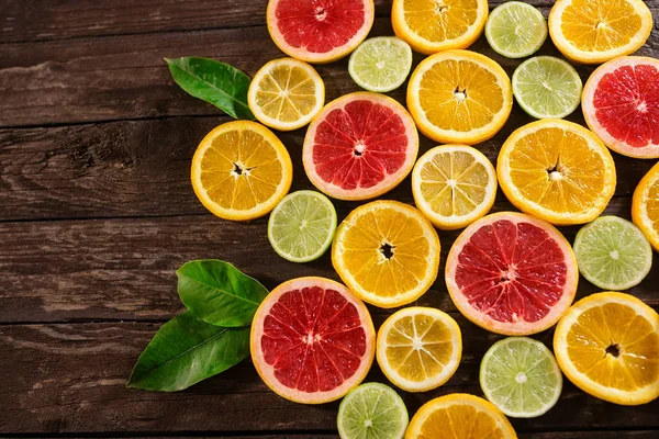 Skiver appelsiner, limefrugter, grapefrugter og citroner. Over træbord - Stock-foto