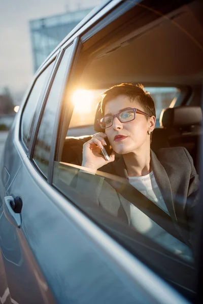 Бизнес-леди ездит в машине и пользуется смартфоном — стоковое фото
