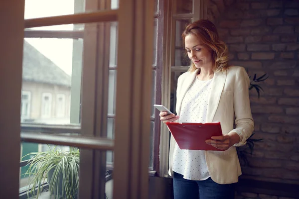 Vrouw zoekt op mobiele telefoon door raam — Stockfoto