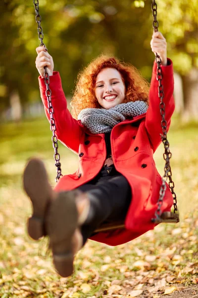 Krullend gember meisje op schommel in park — Stockfoto