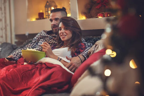 Hombre y mujer en la cama viendo la televisión y comiendo maíz pop — Foto de Stock
