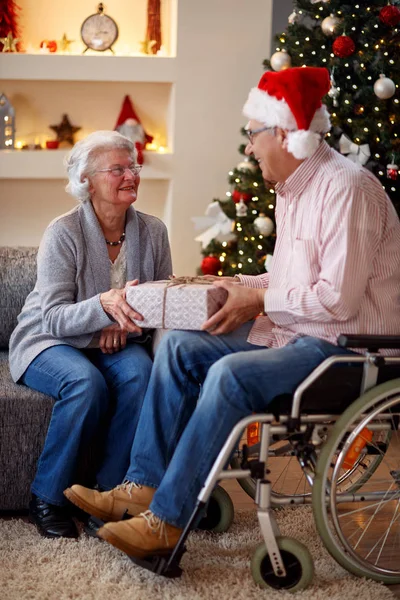 senior man in wheelchair and woman with Christmas gift