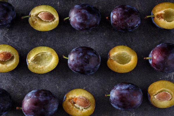 Vue de dessus sur prunes juteuses, entières et tranches sur fond sombre — Photo