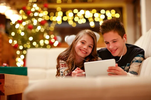 Niño y niña con auriculares acostados y usando una tableta para Navidad —  Fotos de Stock