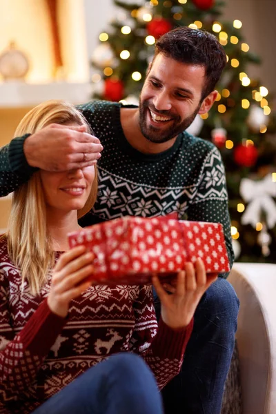 Smiling man covering woman's eyes with hands and giving gift box — Stock Photo, Image