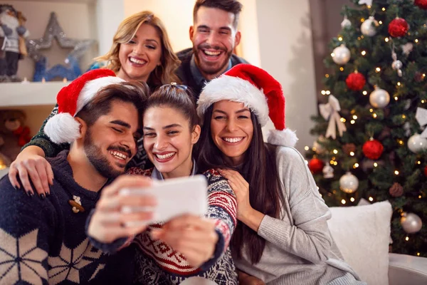 Amigos sonrientes felices tomando fotos con el teléfono móvil para Navidad —  Fotos de Stock