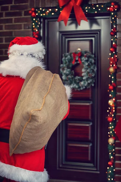 Santa Claus with big sack in front of home, back view — Stock Photo, Image