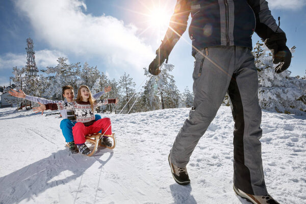 Boy and girl sitting on sleds and father pulling them