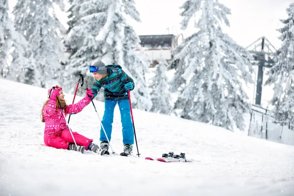 Niño ayuda a chica a levantarse de la nieve con esquís —  Fotos de Stock
