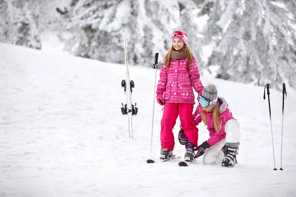 Madre ayuda a su hija a poner correctamente zapatos de esquí en los esquís —  Fotos de Stock