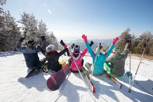 Joyeux skieurs assis sur la neige en montagne, vue arrière — Photo