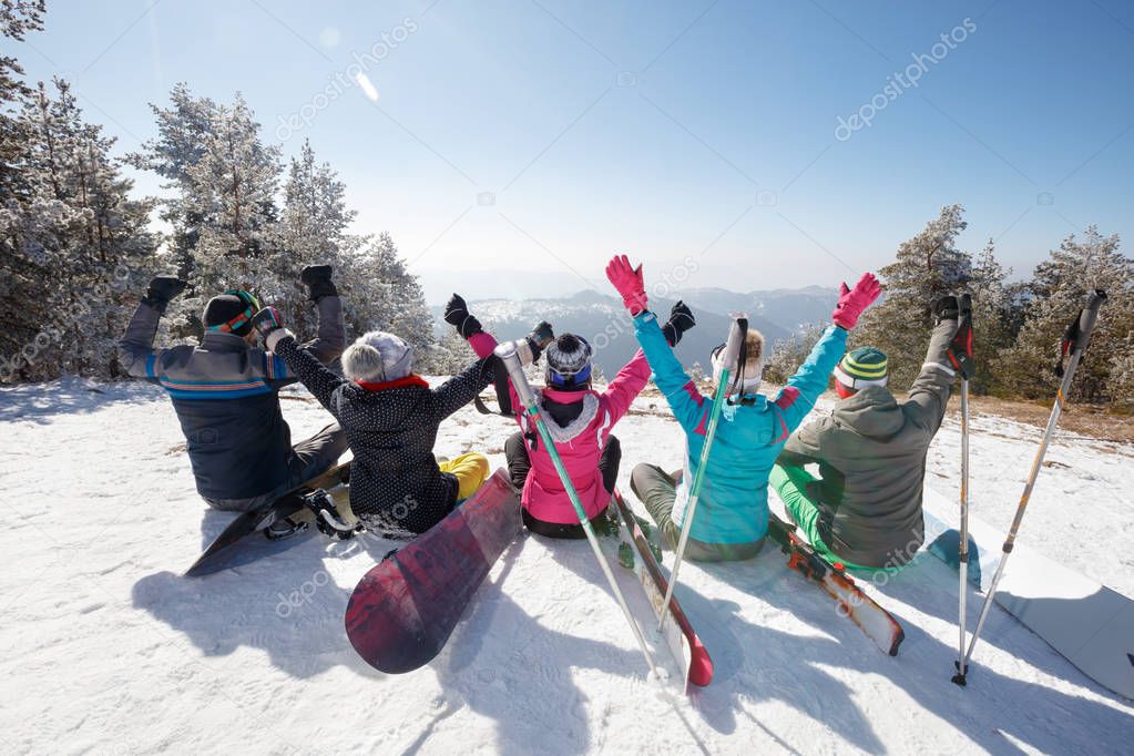 Happy skiers sitting on snow in mountain, back view