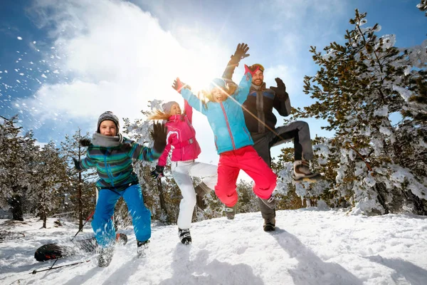 Семья с детьми прыгает в высоту в зимний день на лыжном отдыхе и веселится — стоковое фото