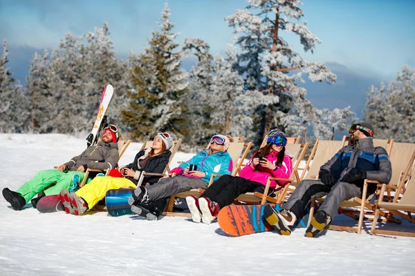 Amigos sentados com espreguiçadeiras em montanhas de inverno. Banho de sol — Fotografia de Stock