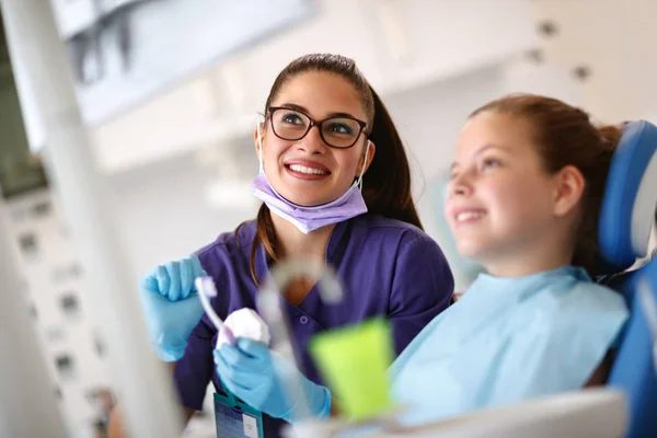 Lächelnde Zahnärztin mit jungem Mädchen im Zahnarztstuhl, die gemeinsam ihre zahnärztliche Röntgenaufnahme betrachten — Stockfoto