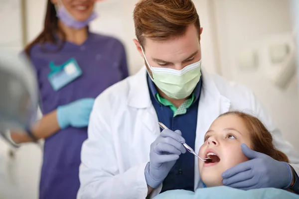 Odontólogo masculino mirando con los dientes del niño espejo dental — Foto de Stock