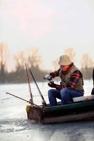 Риболовля льодом. літній чоловік сидить на замерзлому озері і п'є чай — стокове фото