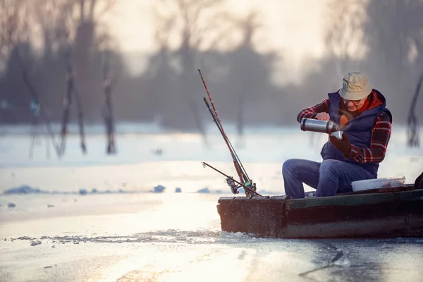 Зимний сезон - пожилой человек сидит на замёрзшем озере и пьет чай — стоковое фото