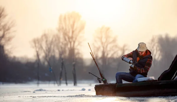 Риболовля на льоду старший чоловік сидить на замерзлому озері і п'є чай — стокове фото