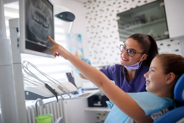 Chica en silla dental mostrando al dentista su diente en rayos X dentales —  Fotos de Stock