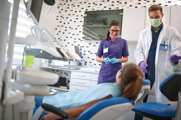 Ассистент стоматолога и врач разговаривают с девушкой в стоматологическом кресле — стоковое фото