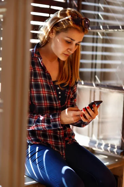 Girl near window looking in cell phone — Stock Photo, Image